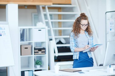 Yaratıcı kadın yönetici evde işyerinin yanında dururken copybook notlar yapma