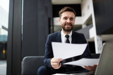 Modern ofiste çalışırken size bakan kağıtları ile Mutlu sakallı işadamı