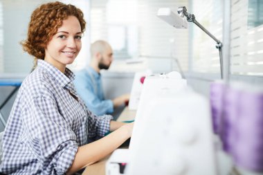 Genç başarılı terzi yeni düzen üzerinde çalışırken dikiş makinesinin yanında oturuyor