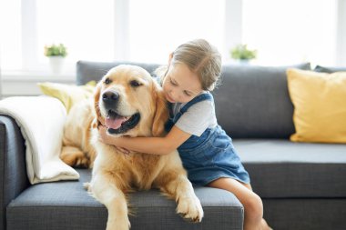 Küçük çocuk evde kanepede rahatlatıcı iken onu labrador evcil hayvan kucaklayan