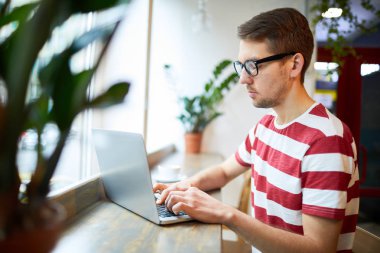 Genç ciddi işadamı pencere eşiğinde otururken ağ kurmaya odaklanıyor