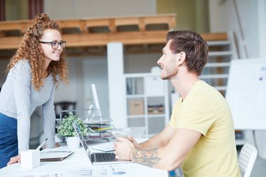 Gündelik giyimli iki genç uzman, iş organizasyonu detayları hakkında masaya oturarak konuşuyor