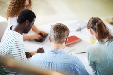 Masa başında oturarak ve bireysel olarak seminere hazırlanan gündelik giyimli genç kültürlerarası öğrenciler grubu
