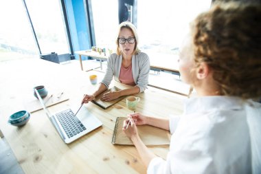 Sanat stüdyosunda ahşap masanın yanında oturan ve net sanat fikirleri ve eğilimleri tartışıyor iki modern yaratıcı kadın