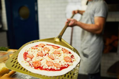 Fırıncı çiğ pizza ile düz metalik tepsi tutarak fırında içine koymak için giderken pişirmek için