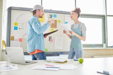 Strateji hakkında beyin fırtınası yaparken ve ofiste yeni bir proje üzerinde çalışırken, gündelik kıyafetler içinde kağıt ve notları görüntüleyen kendinden emin yaratıcı pazarlama ekibi