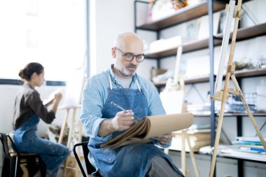 Apron sanat stüdyosunda oturan ve boyama önce not defterinde çizim yaşlı ressam