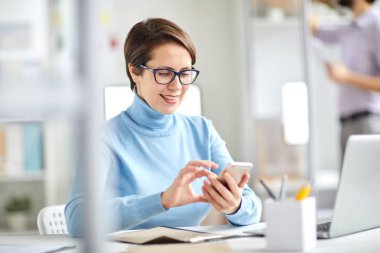Akıllı telefonun masa başında oturması ve mesajlaşması veya molada kaydırma özelliğine sahip modern ofis yöneticisi