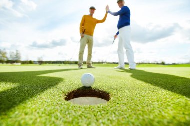 İki aktif erkek oyun alanında ayakta ve delik tarafından Golf topu bakarak, yüksek beş yapma