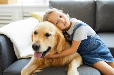 Evde kanepede onun yanında otururken altın labrador kucaklayan sevimli küçük kız