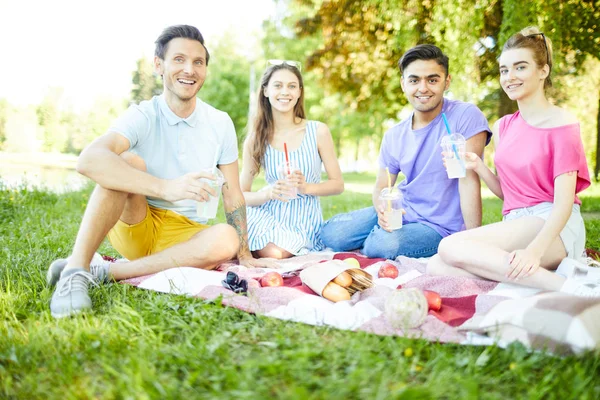 緑の芝生でリラックスし 夏の日にピクニックで飲み物を持っている4人の幸せな十代の若者たち — ストック写真