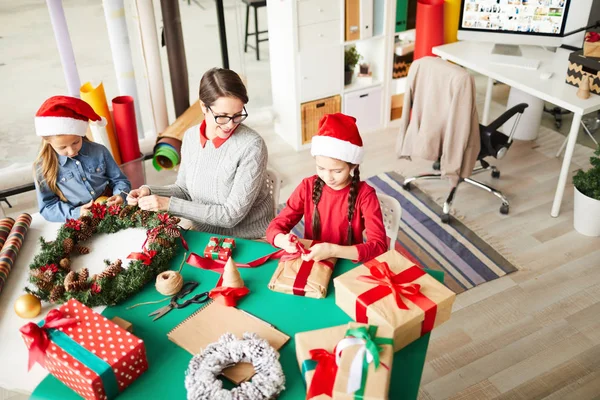 テーブルのそばに座って 今後のクリスマスのための装飾や贈り物を準備する3人の家族 — ストック写真