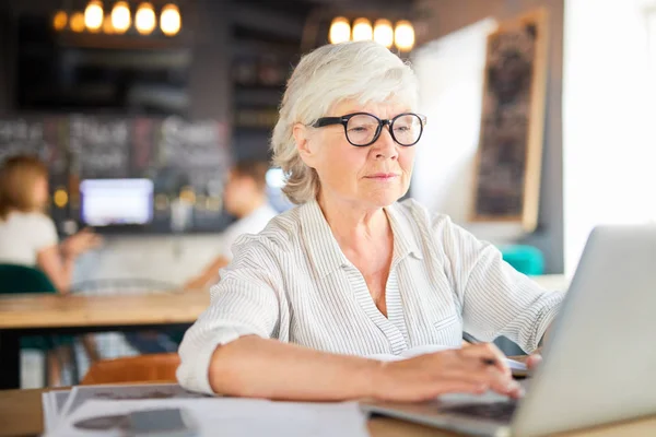 Starszy Siwy Bizneswoman Siedząc Kawiarni Znajdującej Się Naprzeciwko Laptopa Wpisując — Zdjęcie stockowe