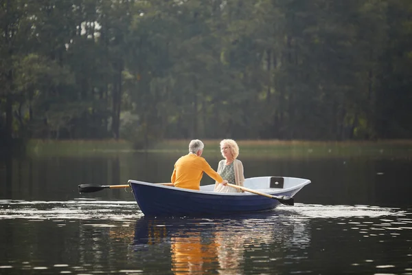 ボートに座って 彼はオールを漕いでいる間に彼氏に話をするカーディガンで美しい巻き毛の年配の女性を笑顔 — ストック写真