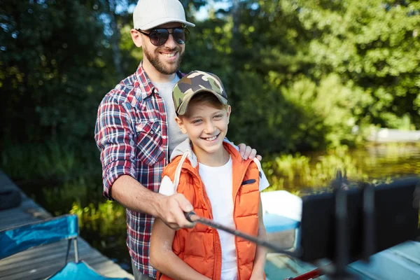 父亲戴着太阳镜 戴着帽子 在湖上和他快乐的儿子合影 — 图库照片