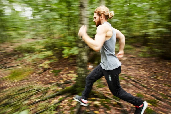 Young sportsman moving forwards while running in the forest with blurry trees around him