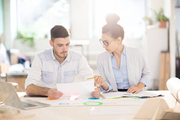 Two young professionals discussing paper and working over new business project at meeting