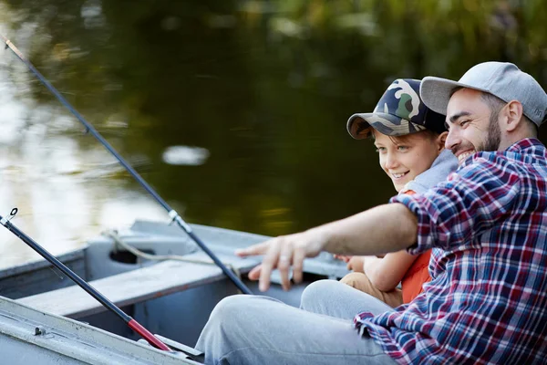 快乐的父亲向他的儿子展示一个很好的地方钓鱼 而他们坐在船上 — 图库照片