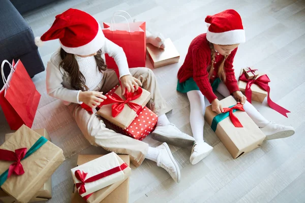 两个戴着圣诞老人帽子的小兄弟姐妹坐在地板上 用圣诞礼物拆开箱子 — 图库照片