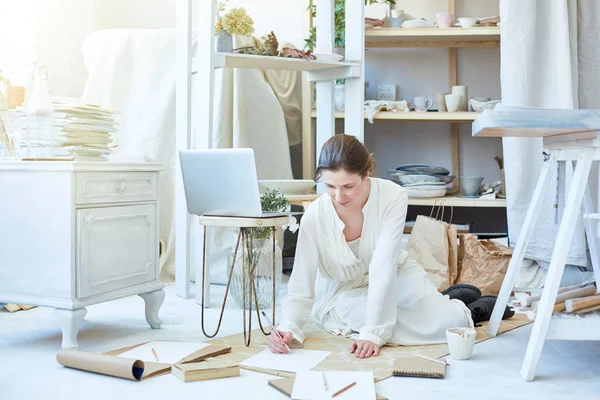 Creative woman sitting gon the floor of her studio and sketching with pencil