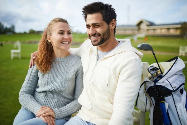 穿着休闲装的快乐年轻夫妇坐在绿地上打高尔夫球和聊天 — 图库照片