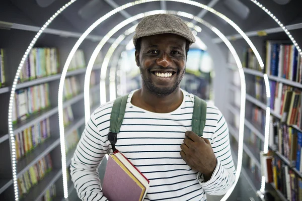 Jonge Lachende Afro Amerikaanse Man Met Pet Casualwear Tussen Boekenplanken — Stockfoto