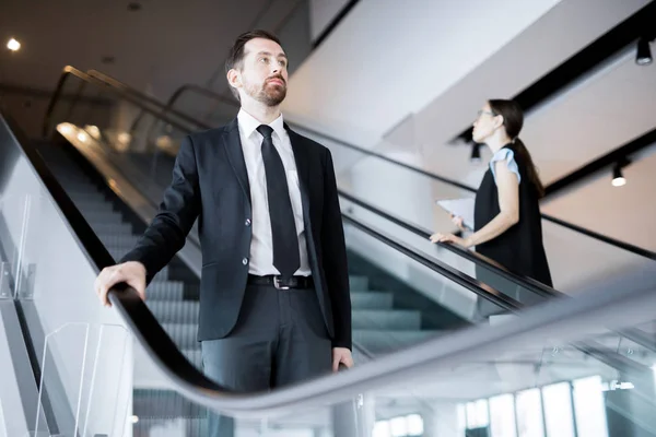 Homem Negócios Sério Movendo Para Baixo Escada Rolante Enquanto Jovem — Fotografia de Stock