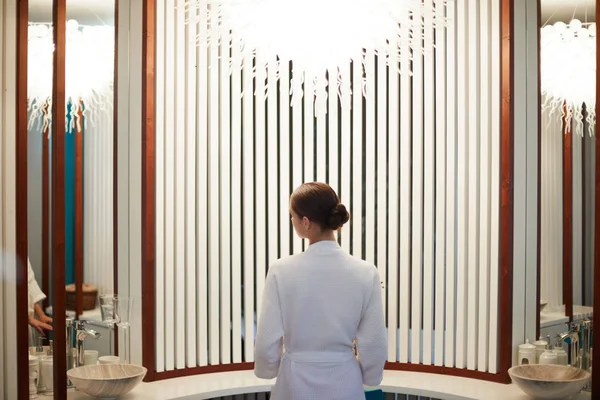 穿着白色浴衣的年轻女子站在豪华水疗室内的后景 — 图库照片