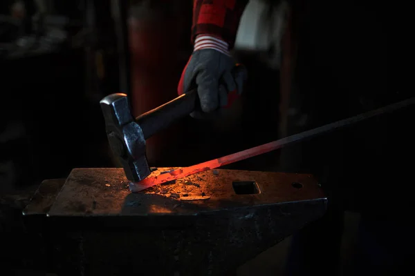 熱い赤い鉄のワークピースとの仕事中にハンマーで鍛冶屋の手袋の手 — ストック写真