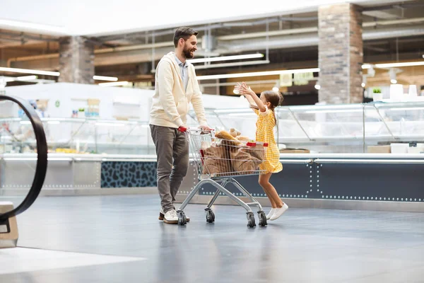 欢快的兴奋可爱的女儿在礼服跳跃与伸出的手臂 同时乞求糖果的父亲或要求父亲抱着她在超市 — 图库照片