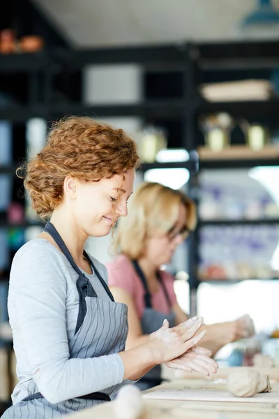 Stüdyoda ya da atölyede çömlekçilik yaparken genç bir kadın, elinde kilden bir parça tutuyor.