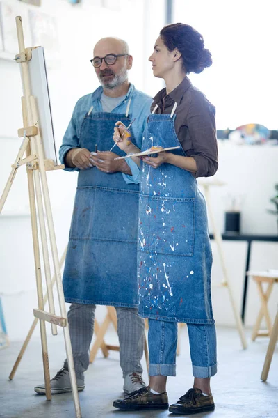 Mature Teacher Looking Easel Young Painter Pointing Out Stuff Should — Stock Photo, Image