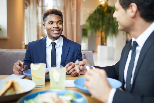 Smiling African businessman has a business lunch together with his colleague, they talking and eating at restaurant