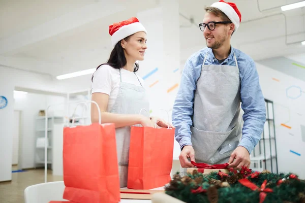 Vrolijke Positieve Jonge Medewerkers Santa Hoeden Schorten Staan Aan Tafel — Stockfoto