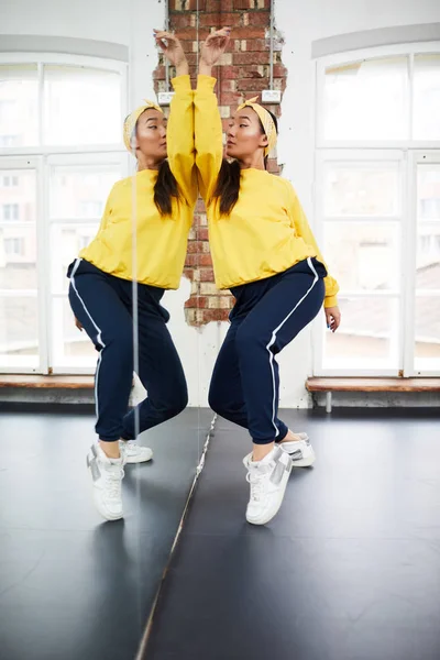 Young professional dancer in activewear training in front of large mirror before performance