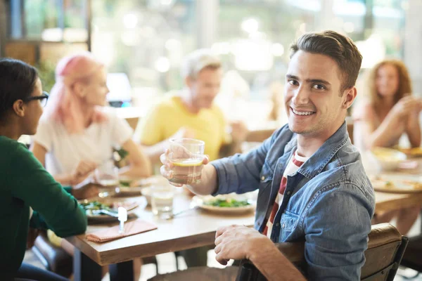 Joven Hombre Sonriente Animándose Con Bebida Mientras Mira Durante Cena —  Fotos de Stock