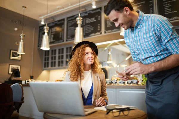 Joven Camarero Anotando Orden Cliente Bastante Elegante Sentado Junto Mesa — Foto de Stock