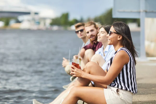 Fila Jovens Amigos Casualwear Tendo Bebidas Enquanto Sentado Beira Mar — Fotografia de Stock