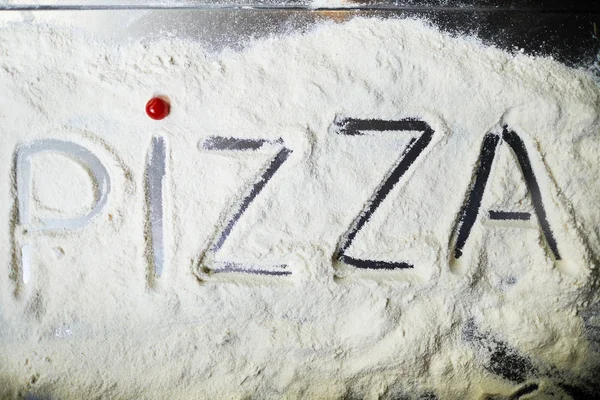 Overview of cooking table surface with flour and word pizza written on it