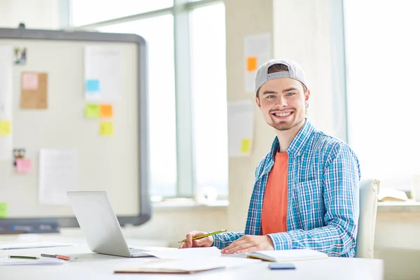 Positive Pleased Handsome Young Intern Cap Sitting Table Learning Literature — Stock Photo, Image