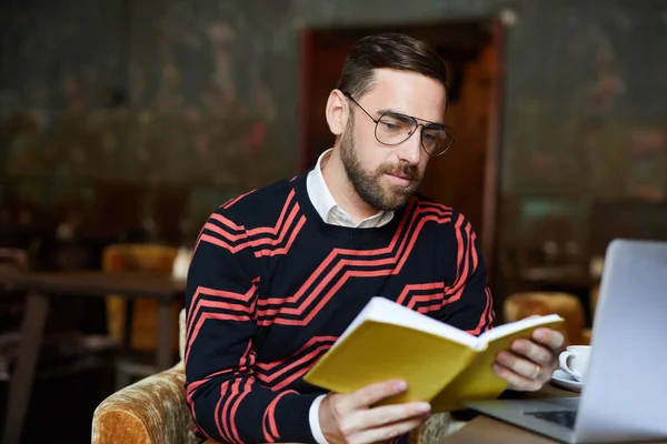 Joven Hombre Serio Gafas Lectura Libro Mientras Pasa Ocio Cafetería — Foto de Stock