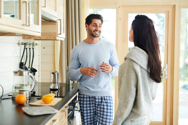 欢快的英俊的年轻胡子丈夫穿着睡衣站在厨房 手势的手 同时与妻子分享故事 他们准备早餐一起 — 图库照片