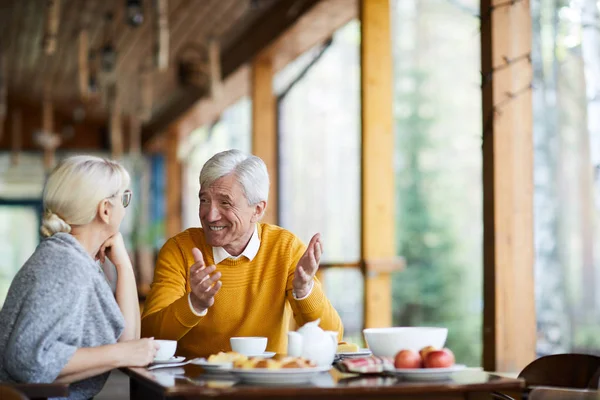 穿着休闲装的白发老人与妻子交谈 而两人都坐在咖啡馆的餐桌旁 — 图库照片