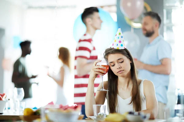 友人を話す背景に彼女の寺院で飲み物とテーブルのそばに座って誕生日キャップの悲しい女の子 — ストック写真