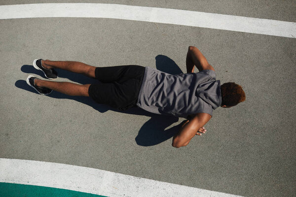 Top view of strong young black man doing push-ups on ground while training at stadium in summer