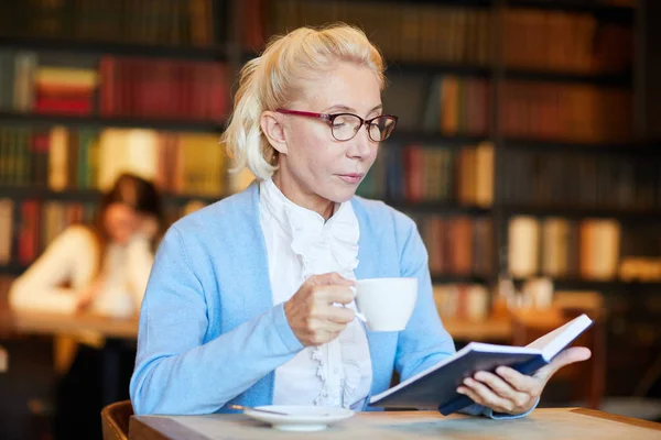 女性で お茶やコーヒーのレジャーで居心地の良いカフェで好奇心が強い小説を読む — ストック写真