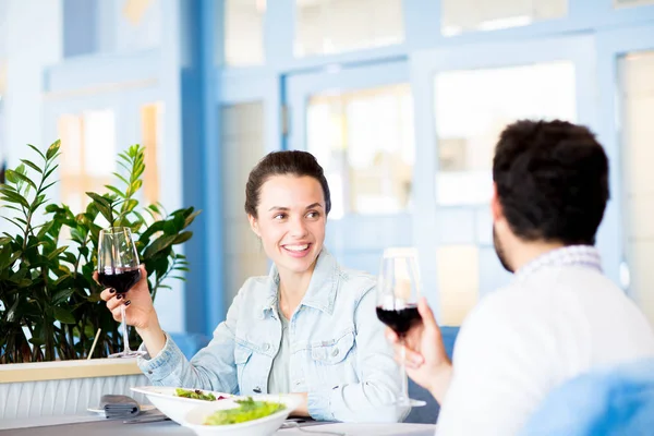 愉快的年轻女子喝着一杯红酒看着她的丈夫 并在餐厅吃午饭时与他交谈 — 图库照片