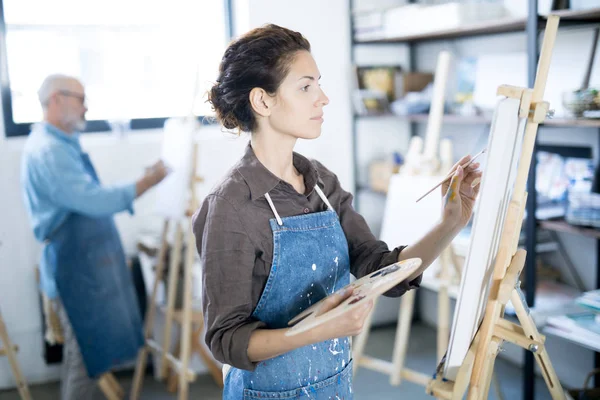 Young Serious Woman Concentrating Painting Picture Easel Her Colleague Background — Stock Photo, Image