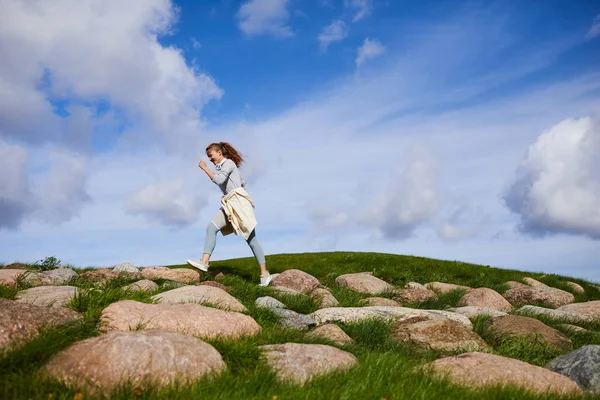 活跃的年轻女子走在大石头对多云的天空在早晨 — 图库照片