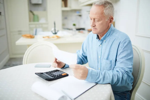 Alter Grauhaariger Mann Liest Finanzzeitung Oder Rechnung Während Tisch Sitzt — Stockfoto